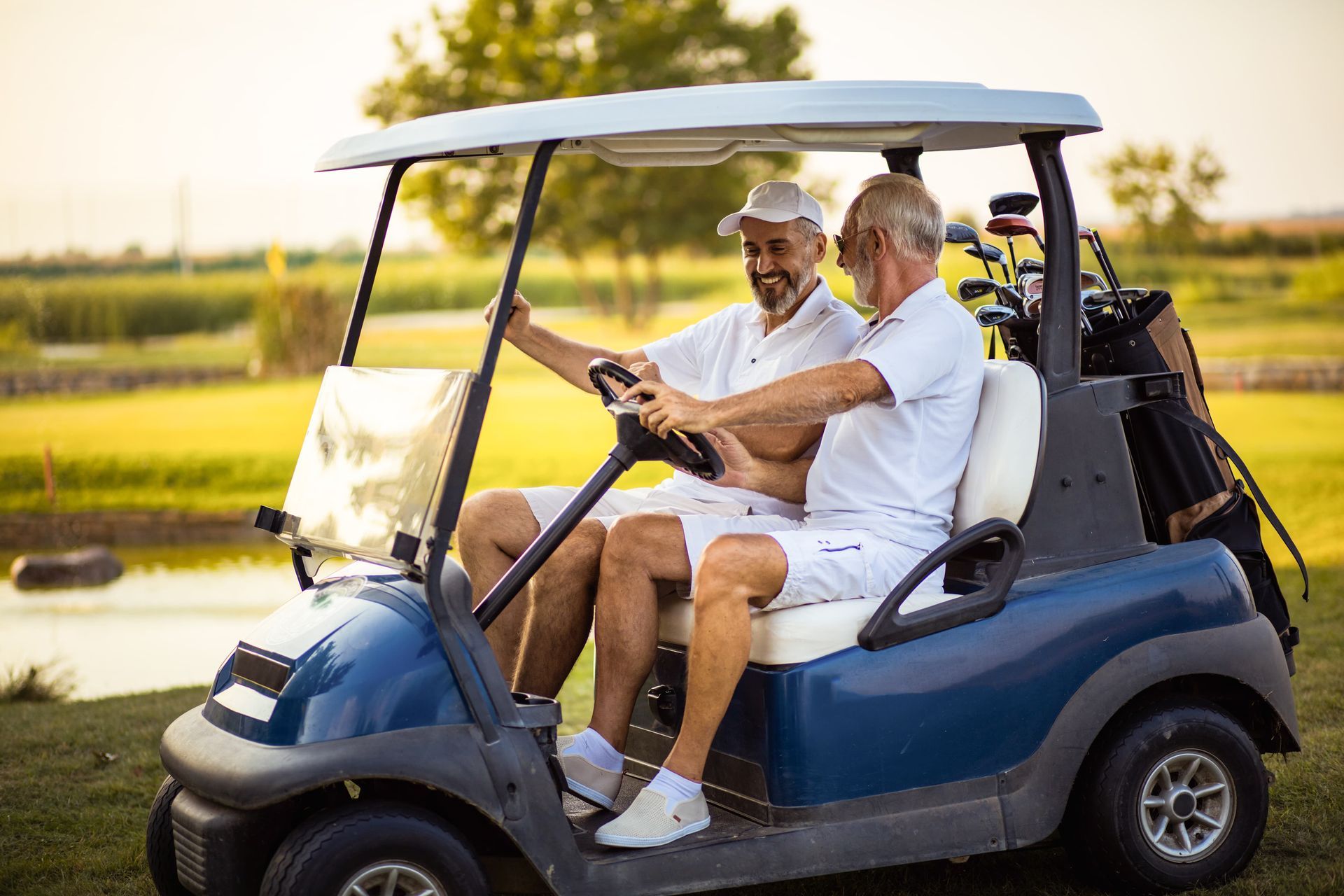 Two people riding a blue golf cart on a grassy path at sunset