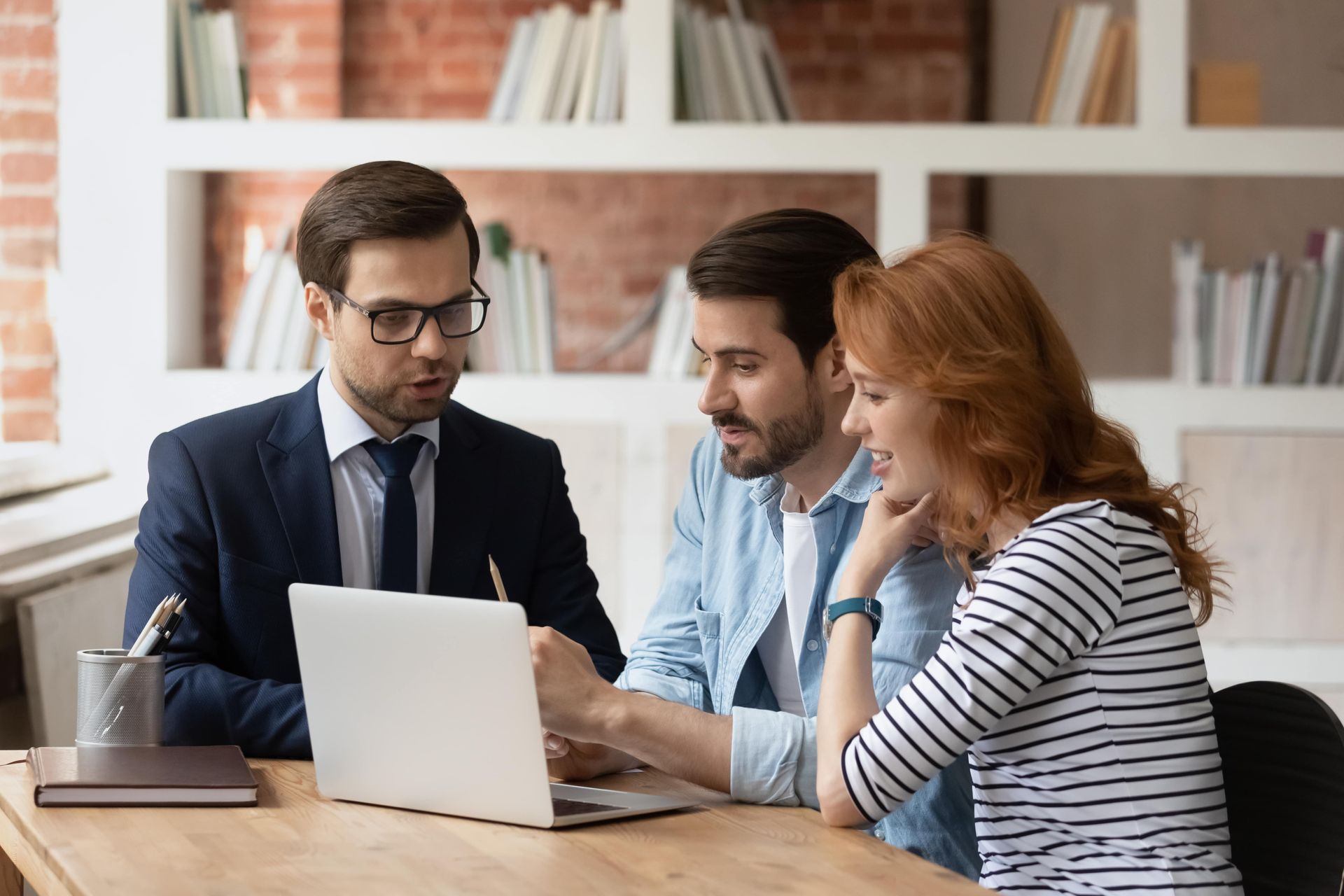 Three coworkers discussing a laptop at a desk in a bright office