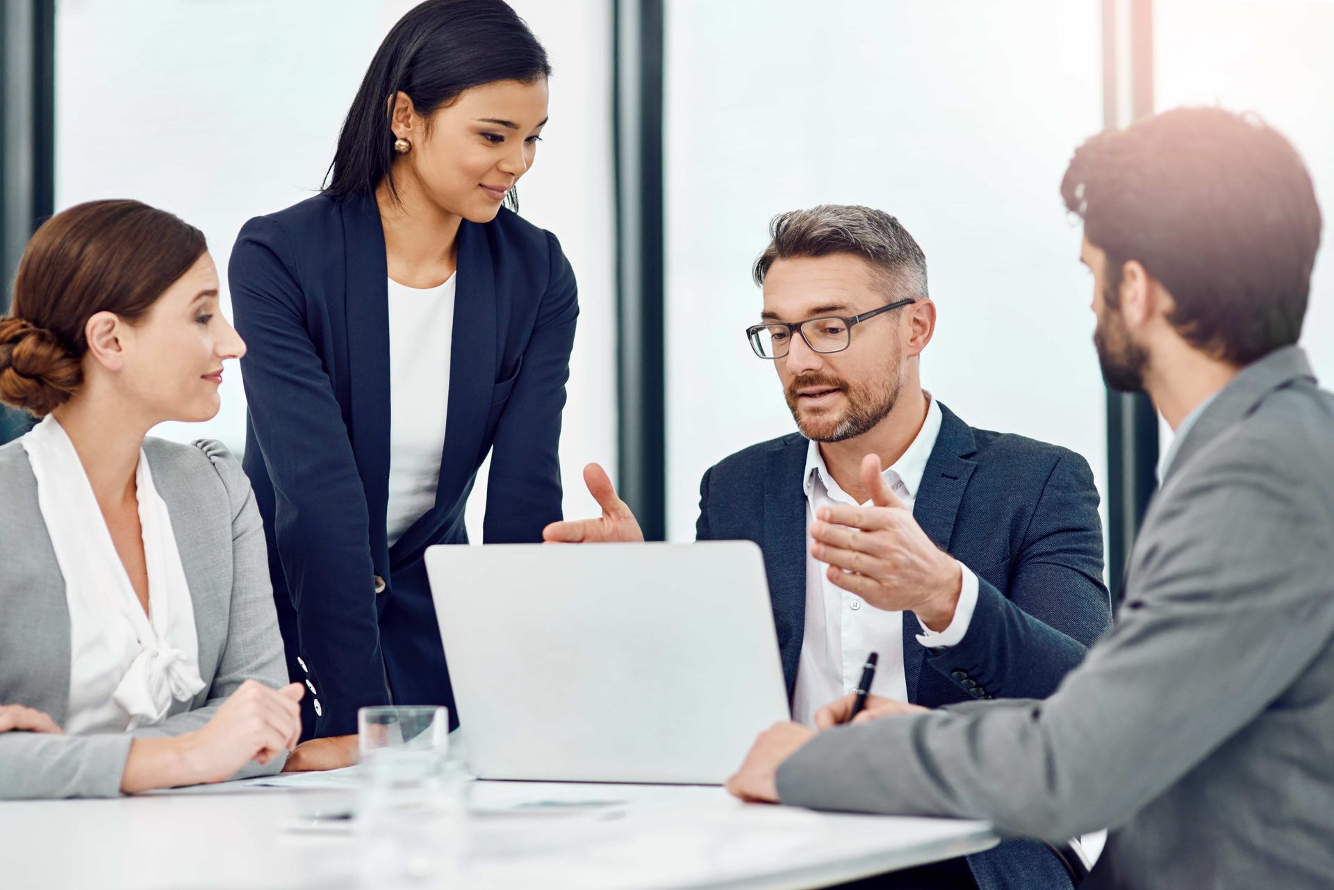 Four coworkers discuss ideas around a laptop in a bright office meeting