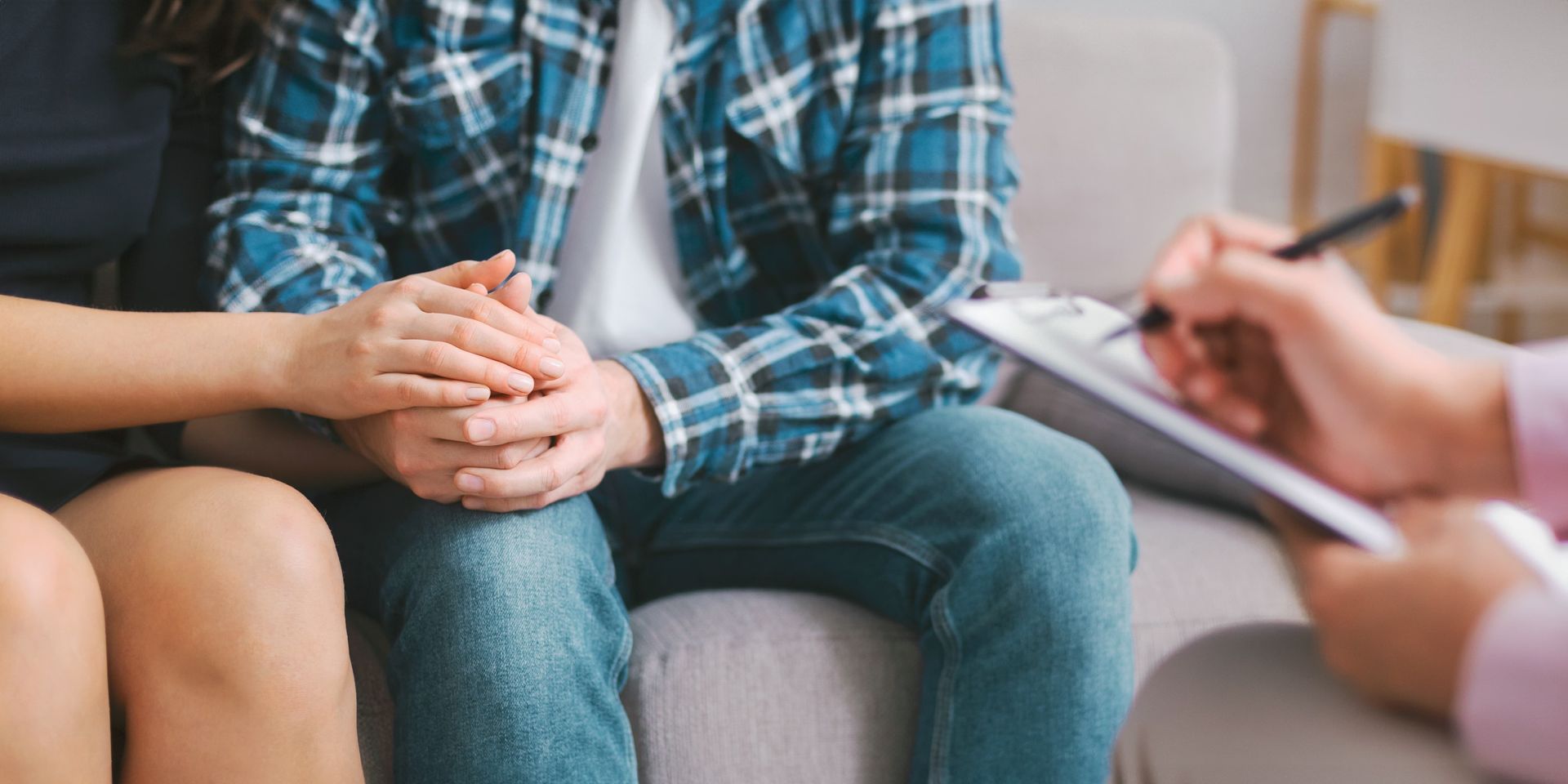 Counselor taking notes while speaking with a seated person in a plaid shirt and jeans