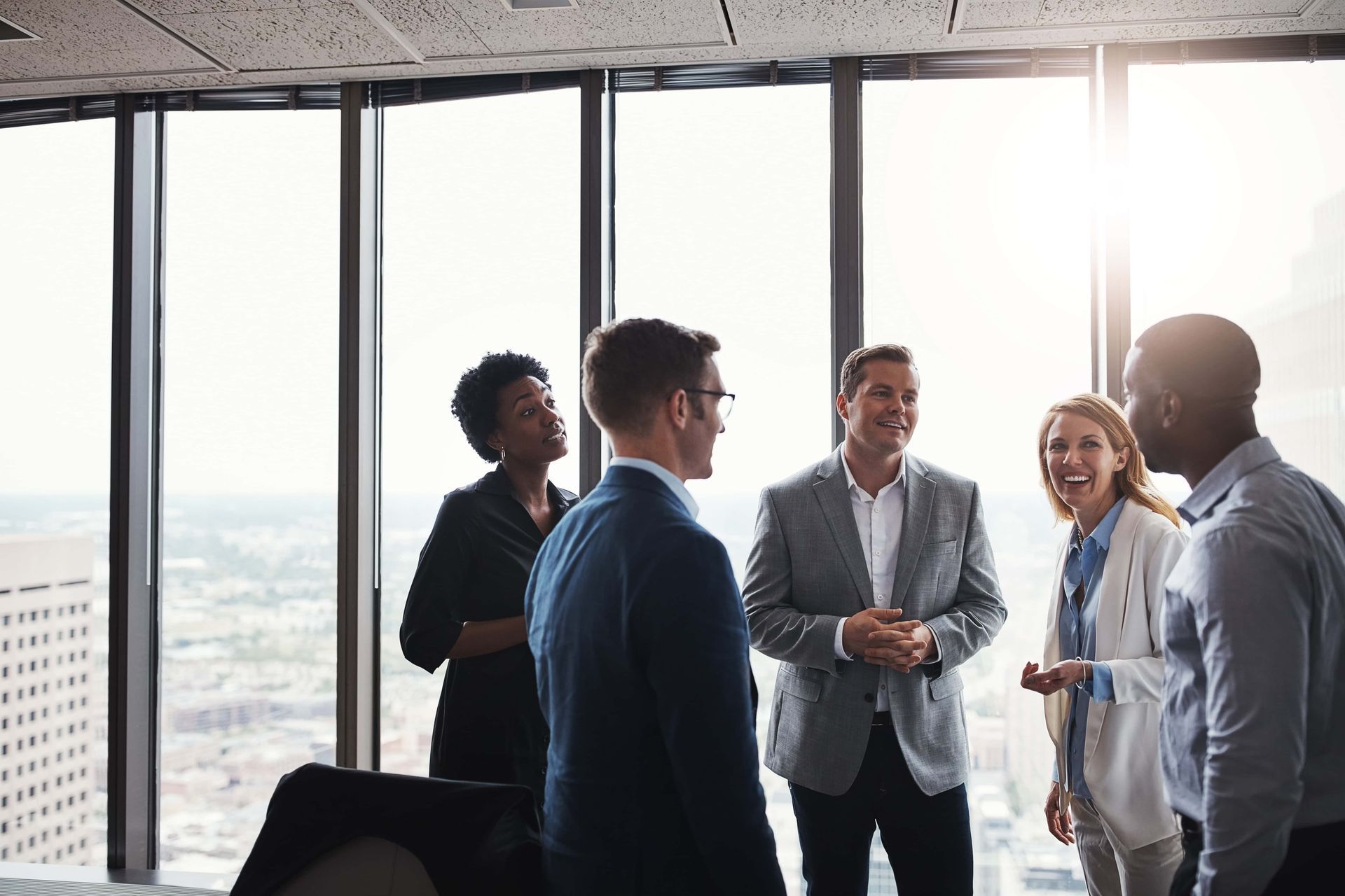 Colleagues talking in a bright office with city windows and sunlight.