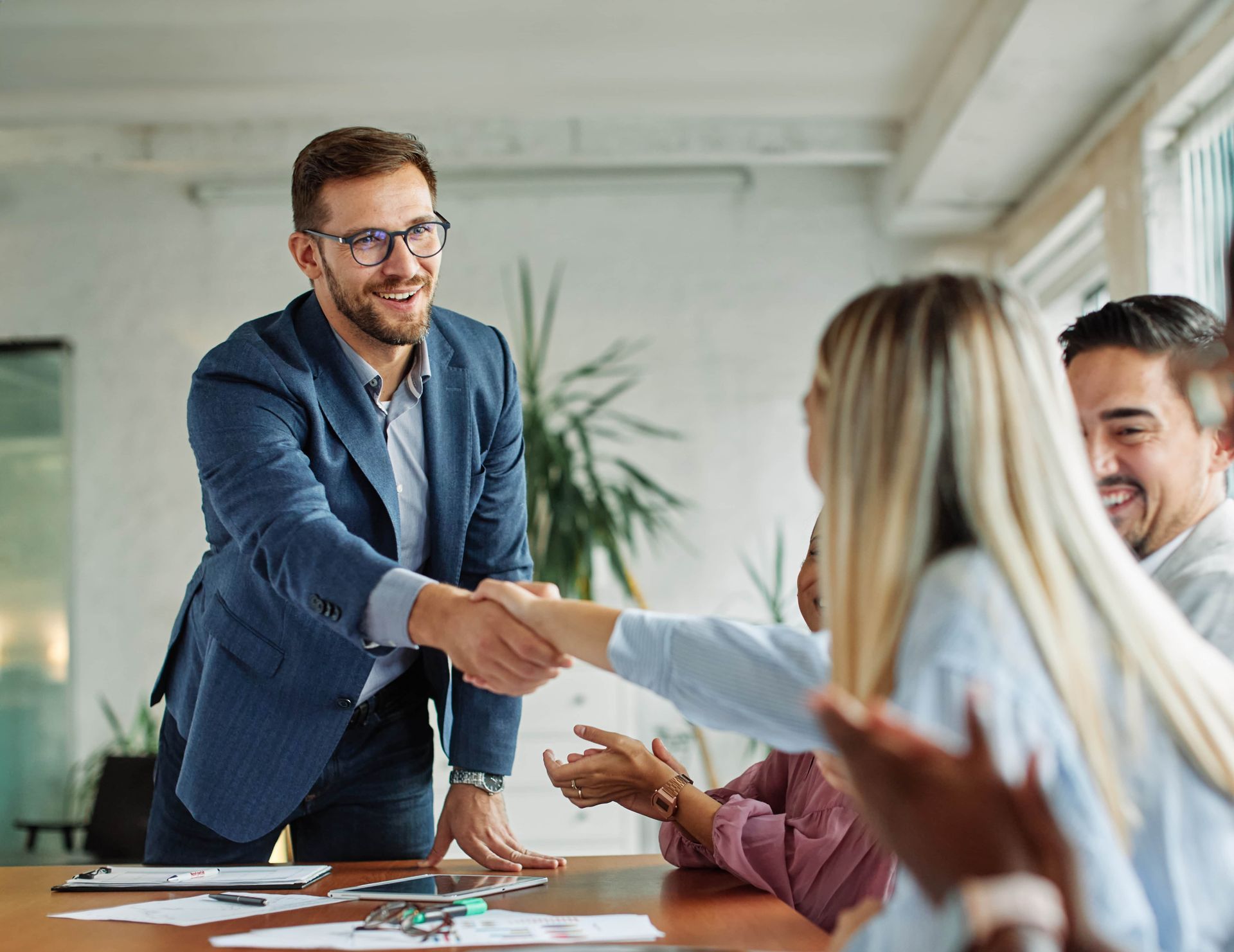 Businessman shaking hands across a conference table in a bright office meeting room