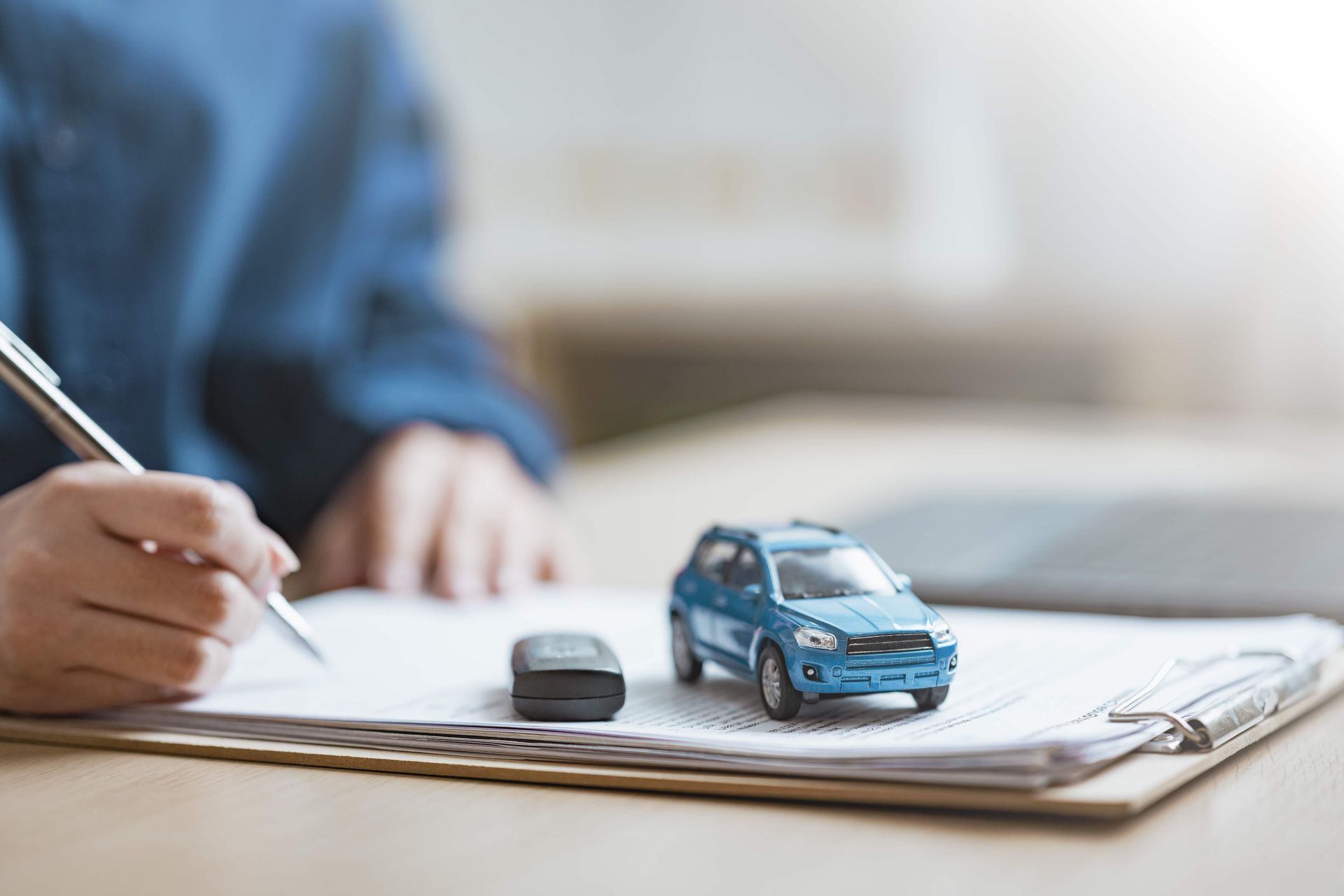 Hand writing on a form beside a toy car and key fob on a clipboard
