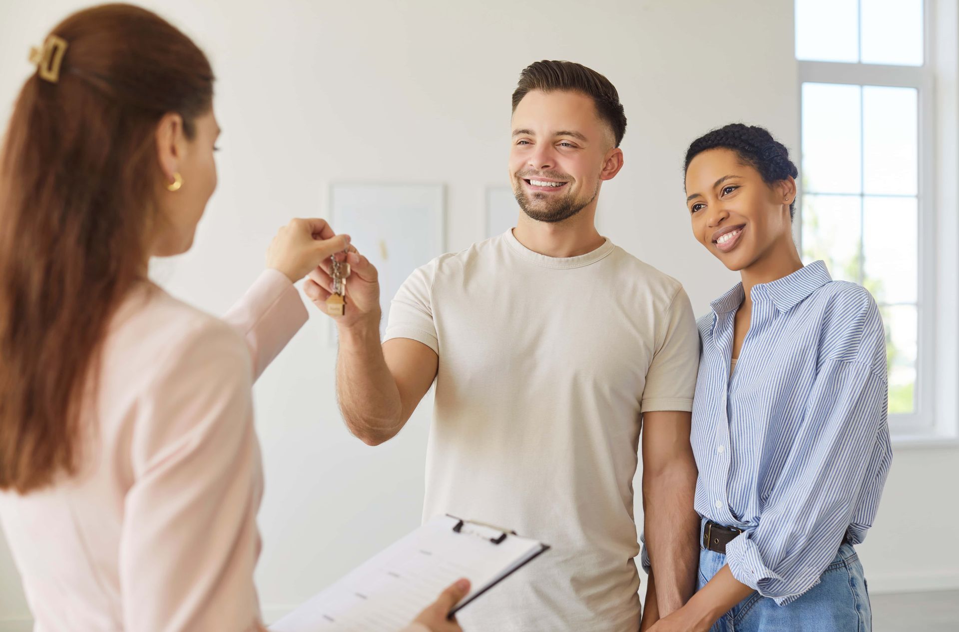 Three people smiling during a home handoff, with one holding keys in a bright room