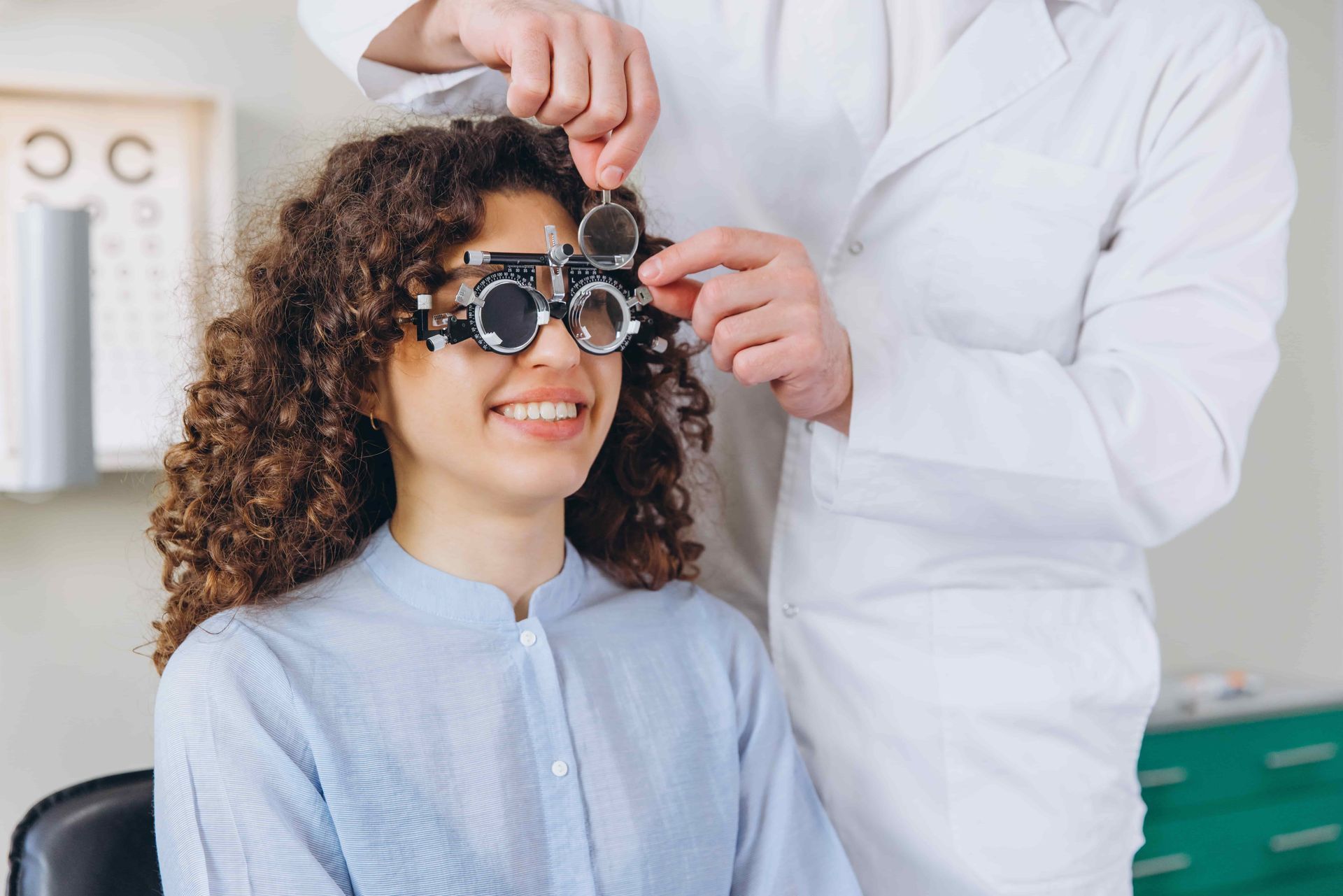 Person in an eye exam chair while an optometrist adjusts trial glasses.