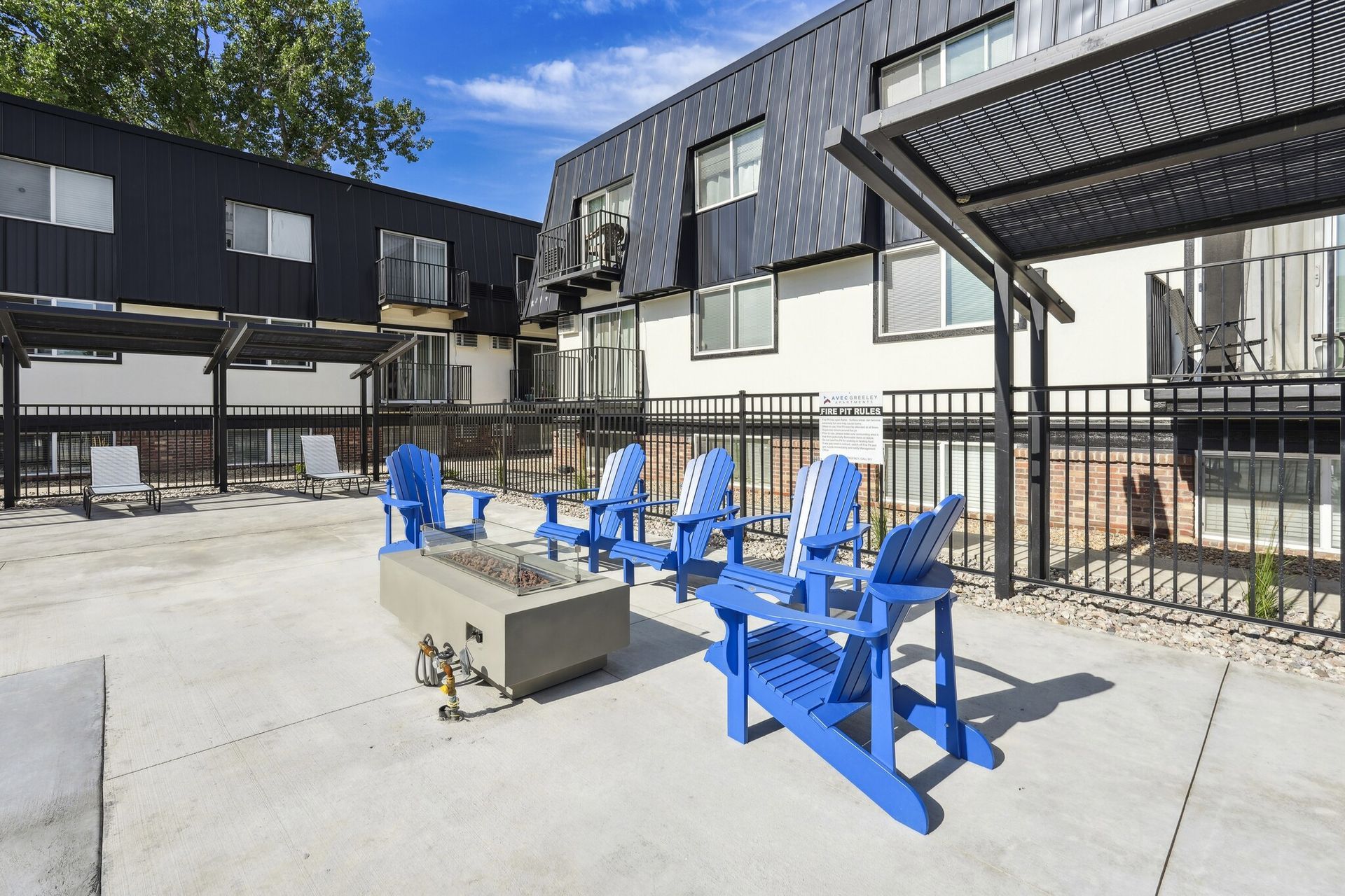 A modern outdoor patio featuring a central fire pit surrounded by several bright blue Adirondack chairs at Avec Greeley.
