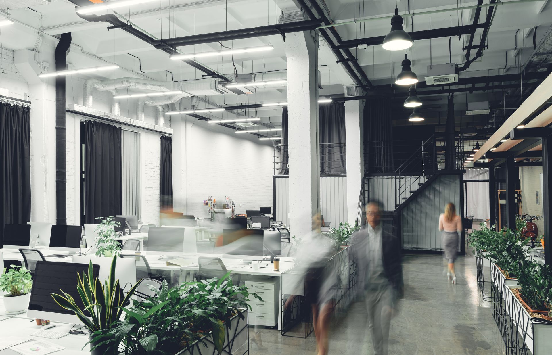 Intérieur de bureau moderne avec des silhouettes floues passant devant des bureaux et de la verdure.