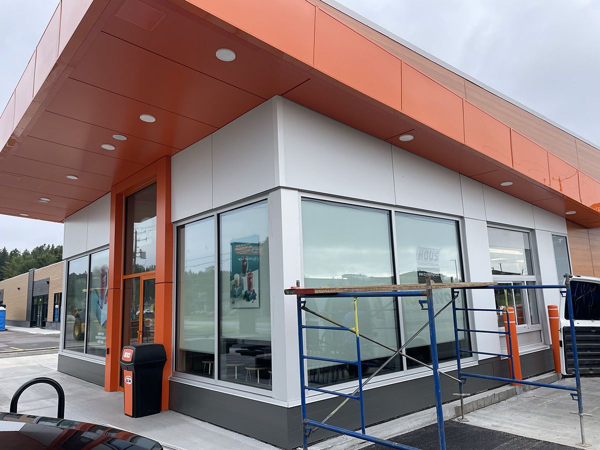 Extérieur d'un bâtiment avec des touches d'orange et de blanc, de grandes fenêtres et des échafaudages.