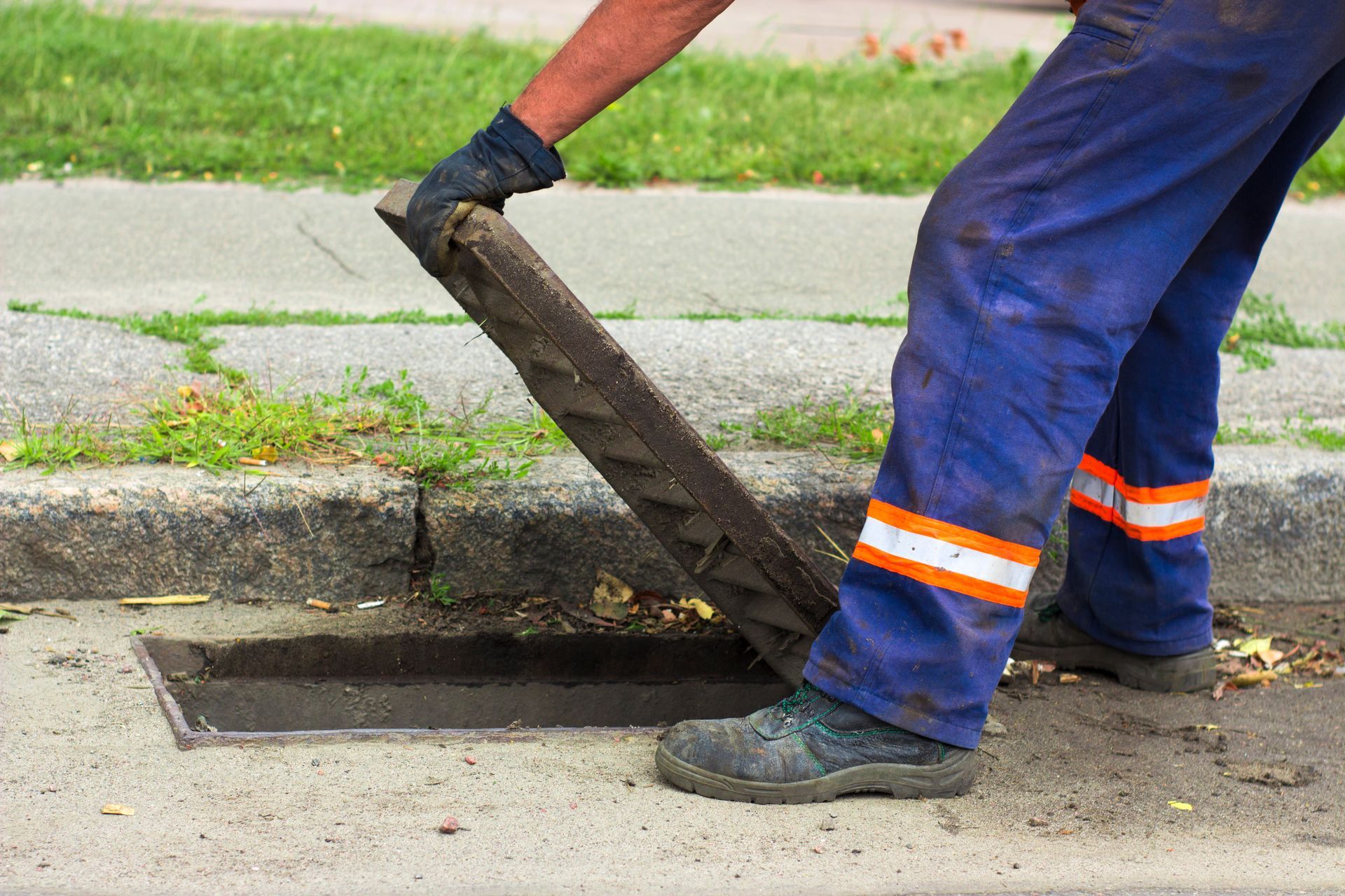 Worker’s hands inspecting drain grate, showcasing sewer line maintenance and professional care.