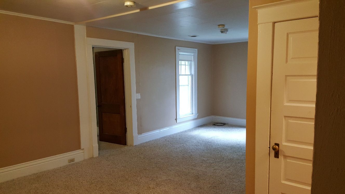Empty room with beige walls, white trim, carpet, a doorway, and a window.