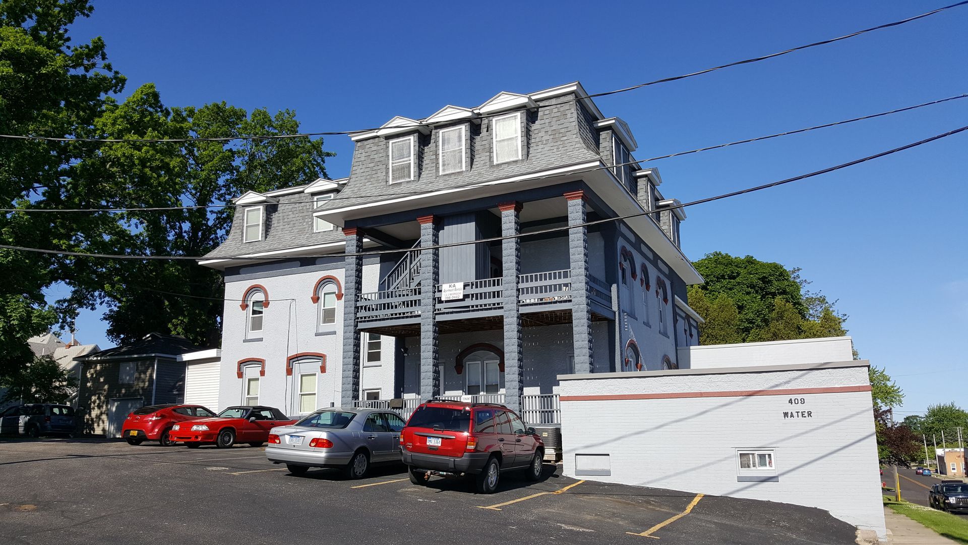 Multi-story gray building with a mansard roof, balconies, and parked cars in front.