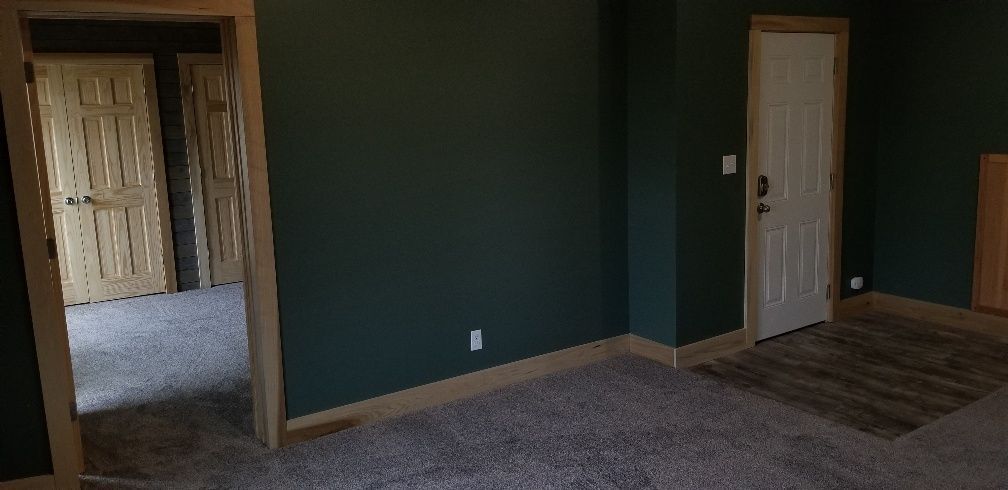 Empty room with dark green walls, white door, and light brown trim. Light gray carpet.