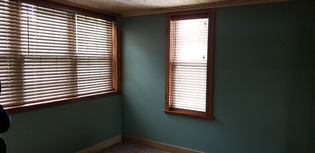 A room with two windows covered by closed blinds. Green walls and brown window frames are visible.