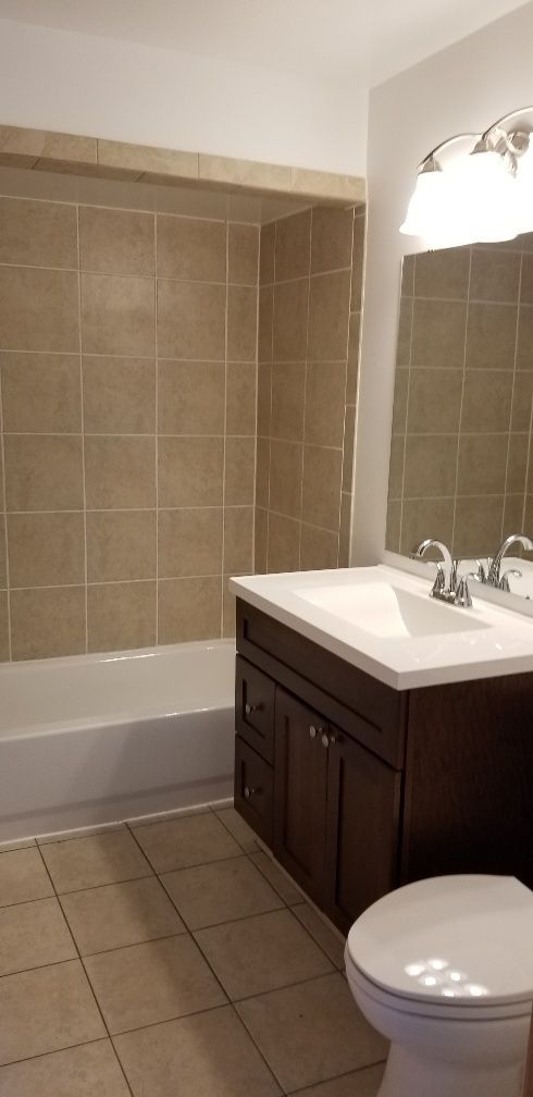Bathroom with a white sink, dark brown cabinets, and beige tile. A white toilet is in the foreground.