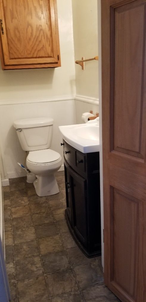 Small bathroom with a toilet, sink, and dark vanity. Wood cabinet above toilet. Brown patterned floor.