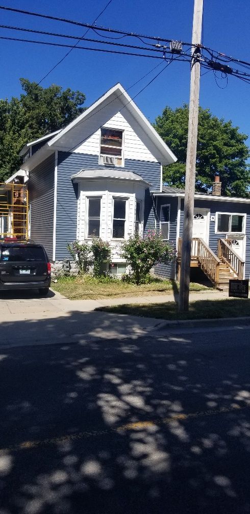 Blue and white house with a dark colored SUV parked on the street. Wooden stairs lead to the right door.