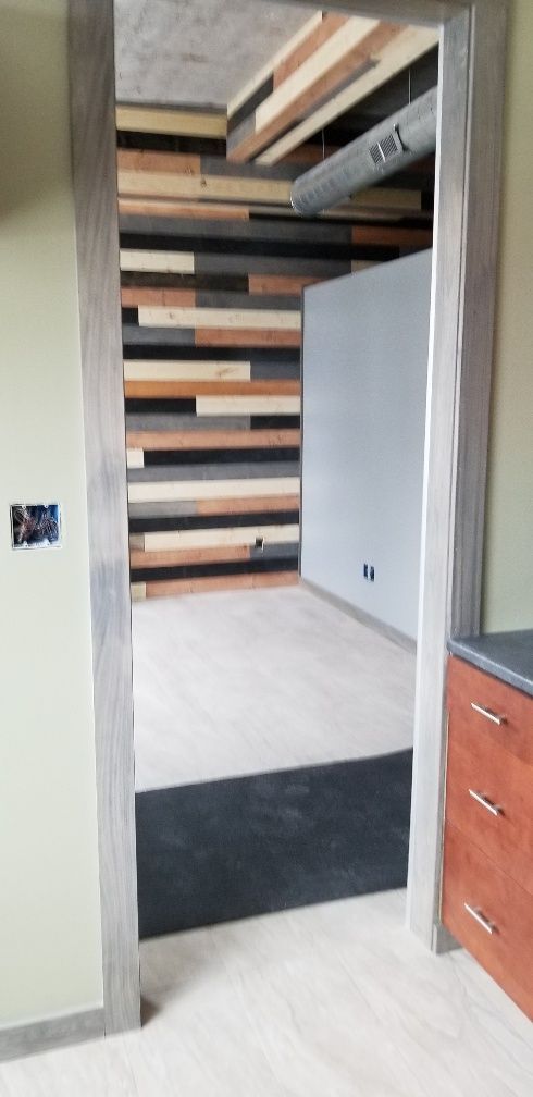 An open doorway with a wood plank wall, floor, and ceiling. Gray trim and a dark mat.