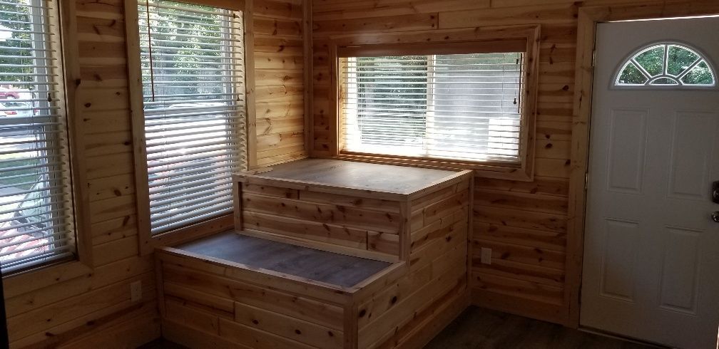 Interior of a wooden cabin with windows, door, and a built-in bench.