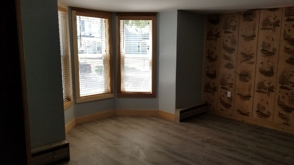 Empty room with bay window, wood-look flooring, and patterned wallpaper.