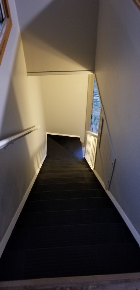 Staircase with black steps, white trim, and gray walls, viewed from the top.
