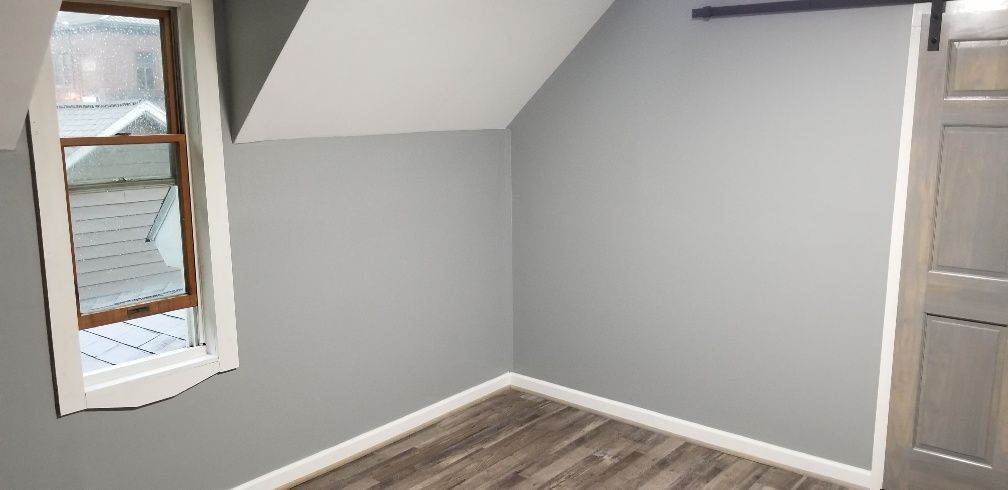 An empty room with gray walls, wood-look floor, window, and barn door. The room has a slanted ceiling.