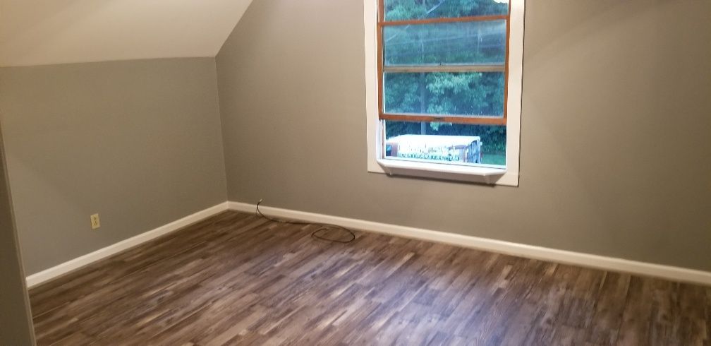 Empty room with gray walls, wooden floor, and a window with a view of the outside.