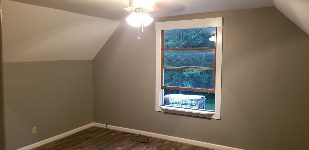 A room with an attic ceiling, a window, and a ceiling fan. The walls are gray, and the window has a white frame.