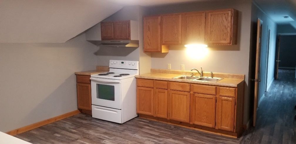 Kitchen with wood cabinets, white stove, and grey flooring.