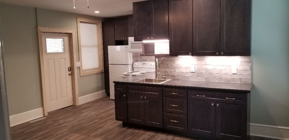 Kitchen with dark cabinets, white appliances, and light-colored walls and door.