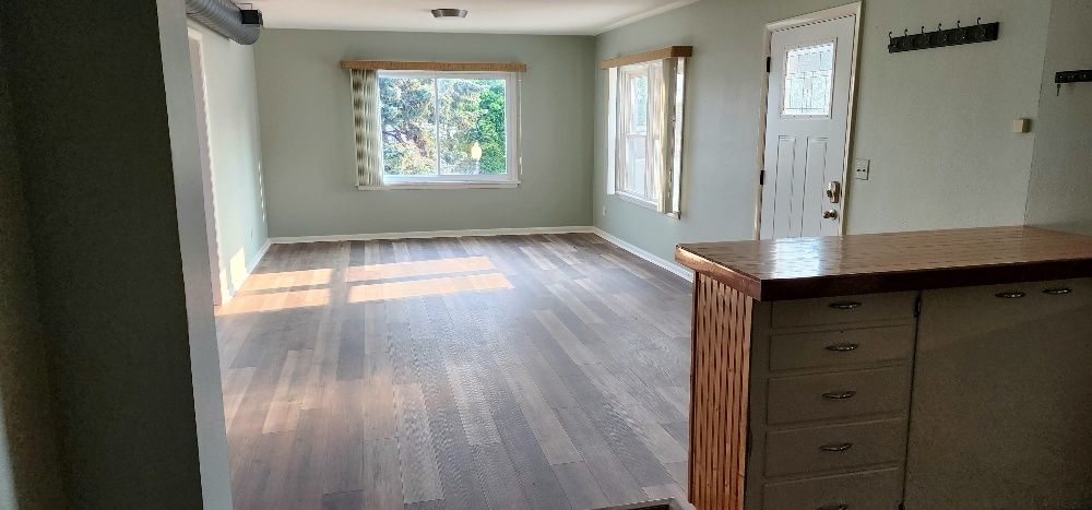 Empty living room with hardwood floors, a window, and a door, partially obscured by a countertop.