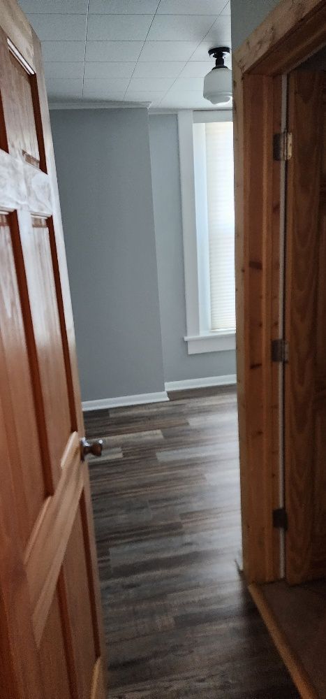 A view from a doorway into a room with gray walls, wood-look flooring, and a window with blinds.