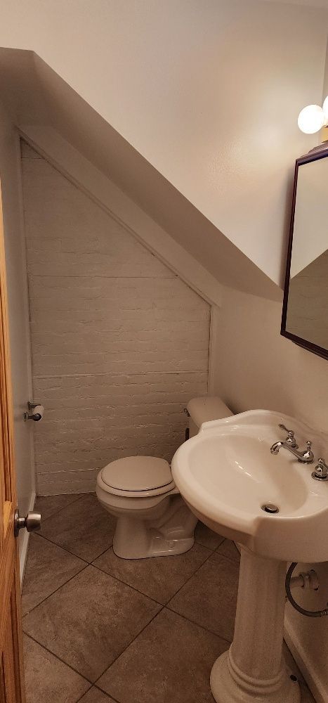 A small bathroom with a toilet, pedestal sink, and angled ceiling. Tile floor.