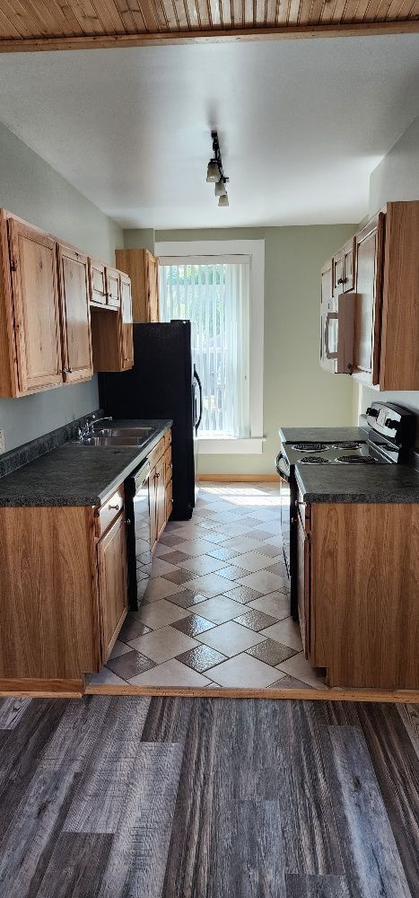 Kitchen with wooden cabinets, dark countertops, and tile and wood flooring. A black refrigerator and stove are also present.