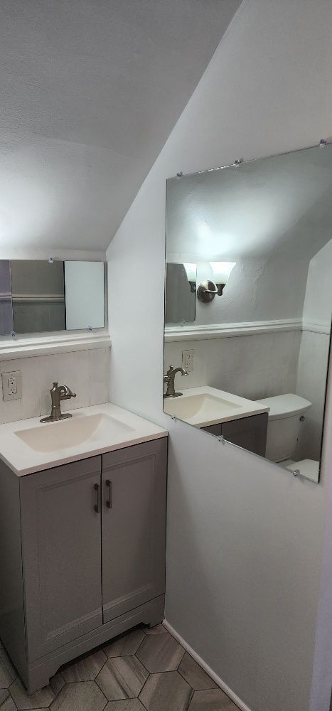 Bathroom with gray vanity, two sinks, and a large mirror reflecting the space.