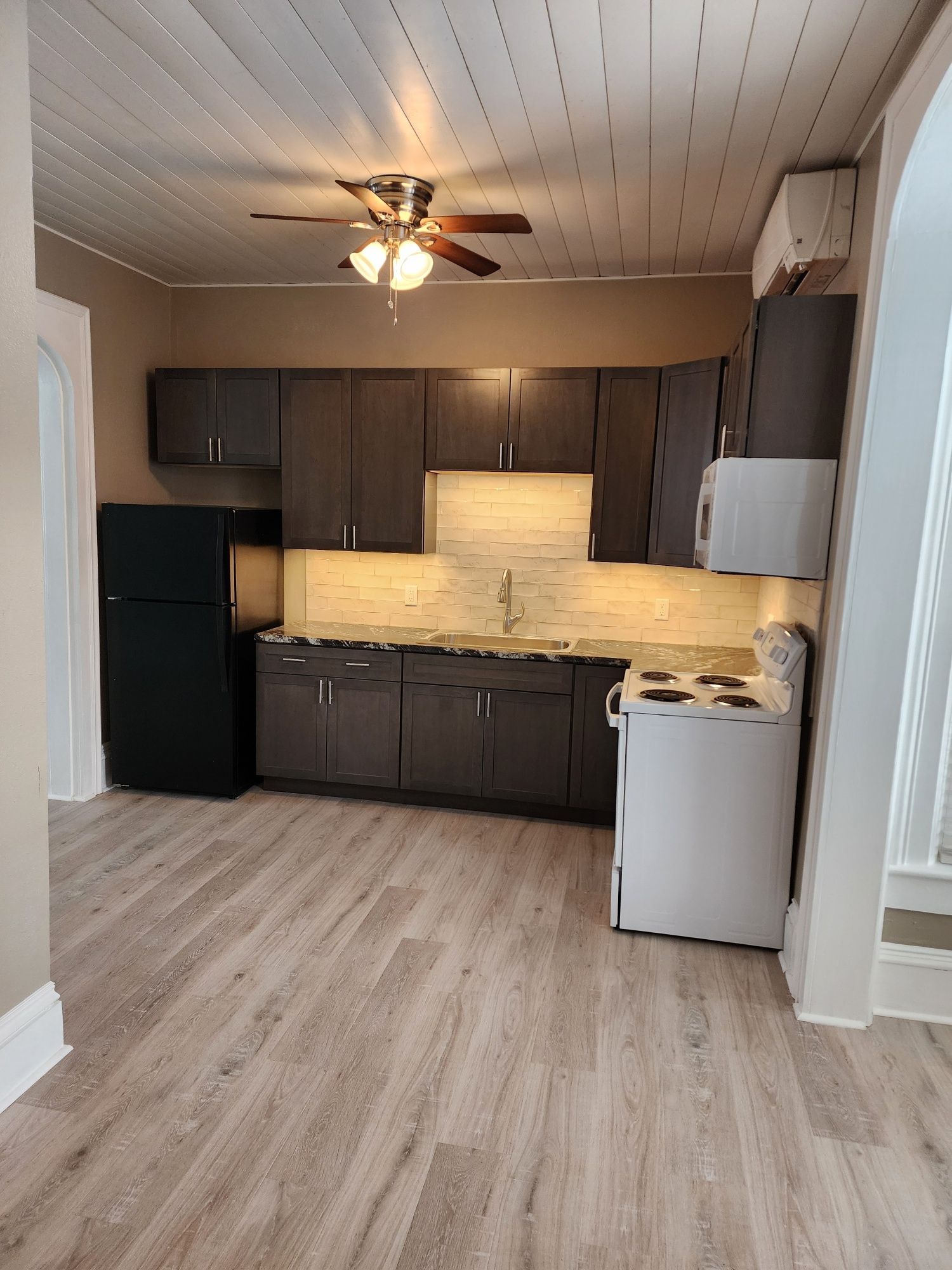 Kitchen with dark cabinets, white appliances, light wood-look flooring, and a ceiling fan.