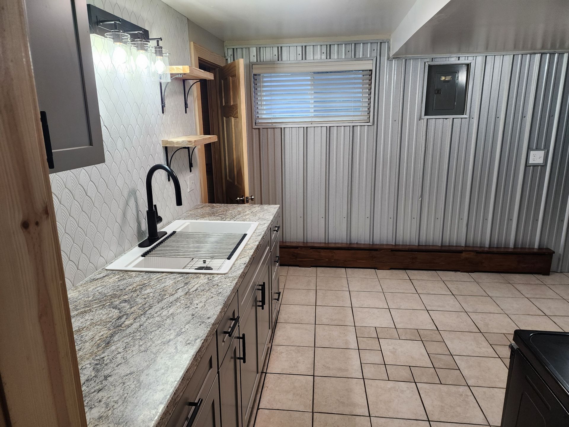 A basement kitchen area with a sink, cabinets, textured walls, and a window.