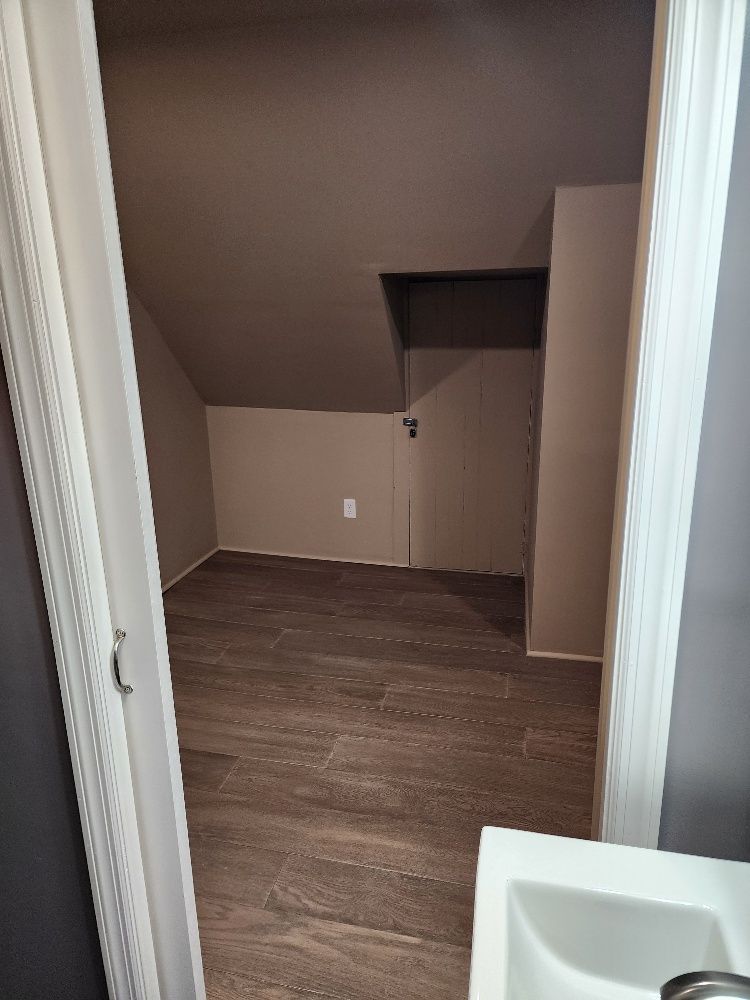 Small, empty room with slanted ceiling, wood-look tile floor, and a doorway.