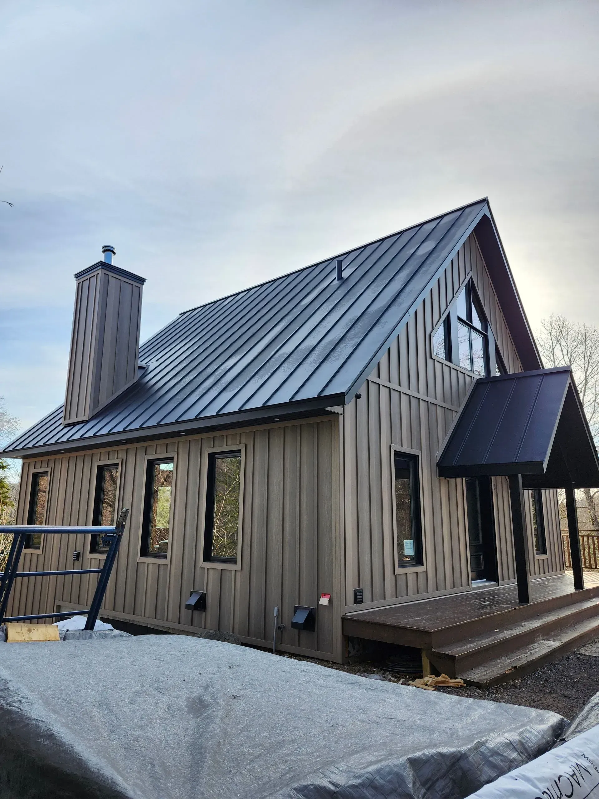 Cabane en bois avec toit métallique pentu et cheminée dans un paysage enneigé au crépuscule