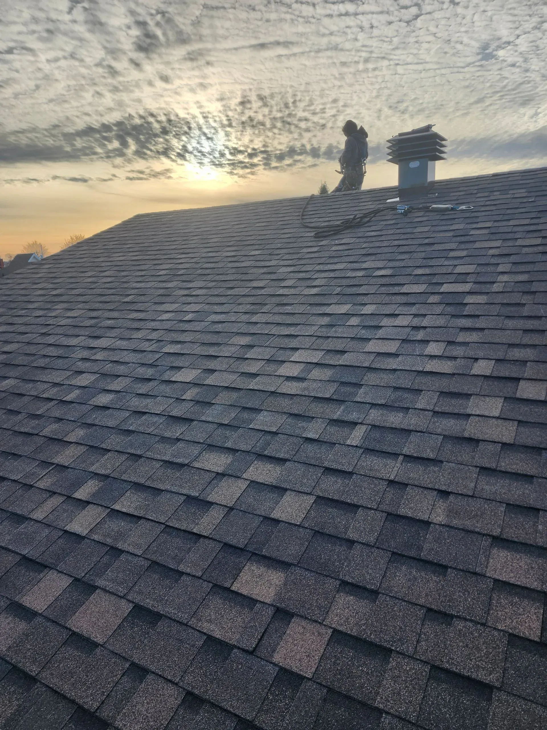 Toiture en tuiles au coucher du soleil, avec deux cheminées se détachant sur un ciel nuageux