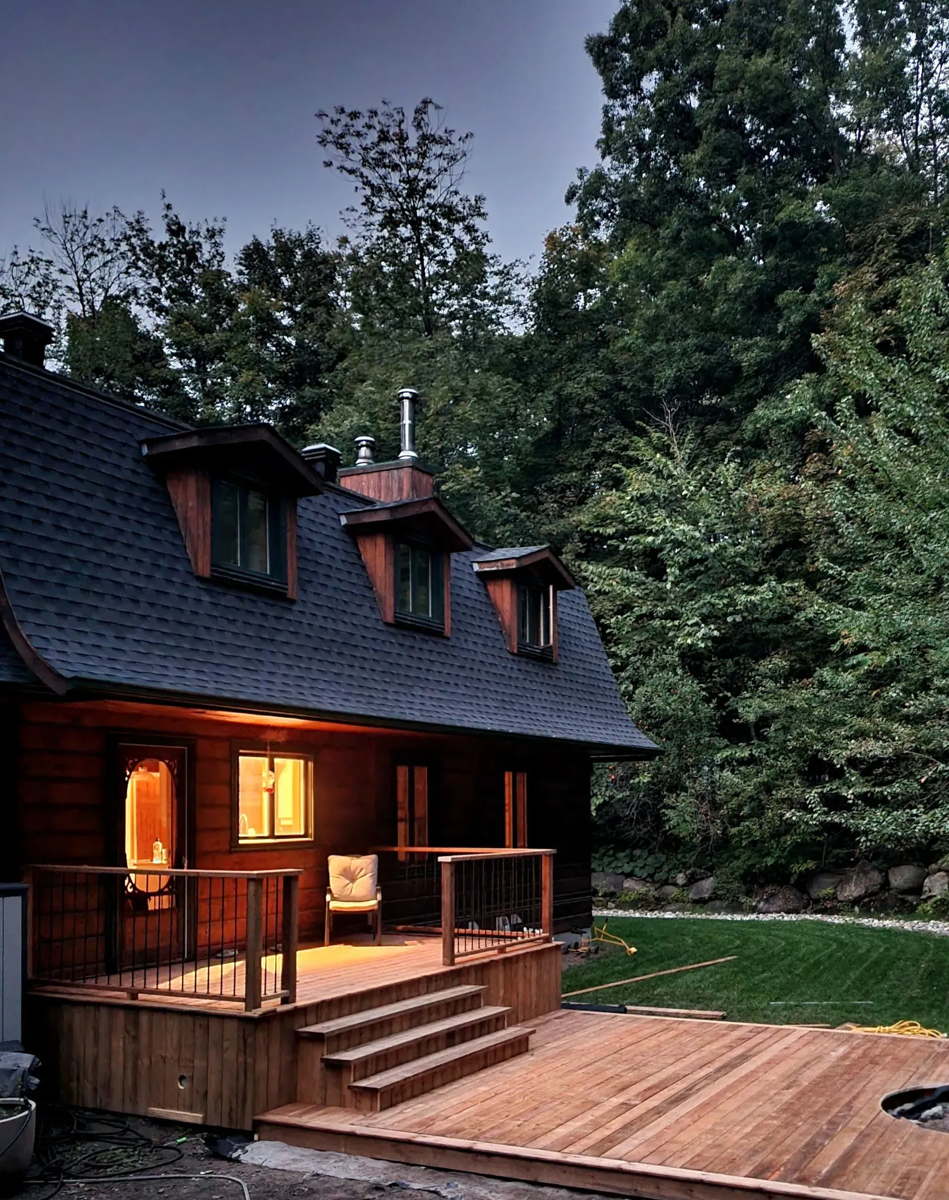 Chalet en bois confortable avec véranda et terrasse éclairées, situé dans un jardin boisé au crépuscule