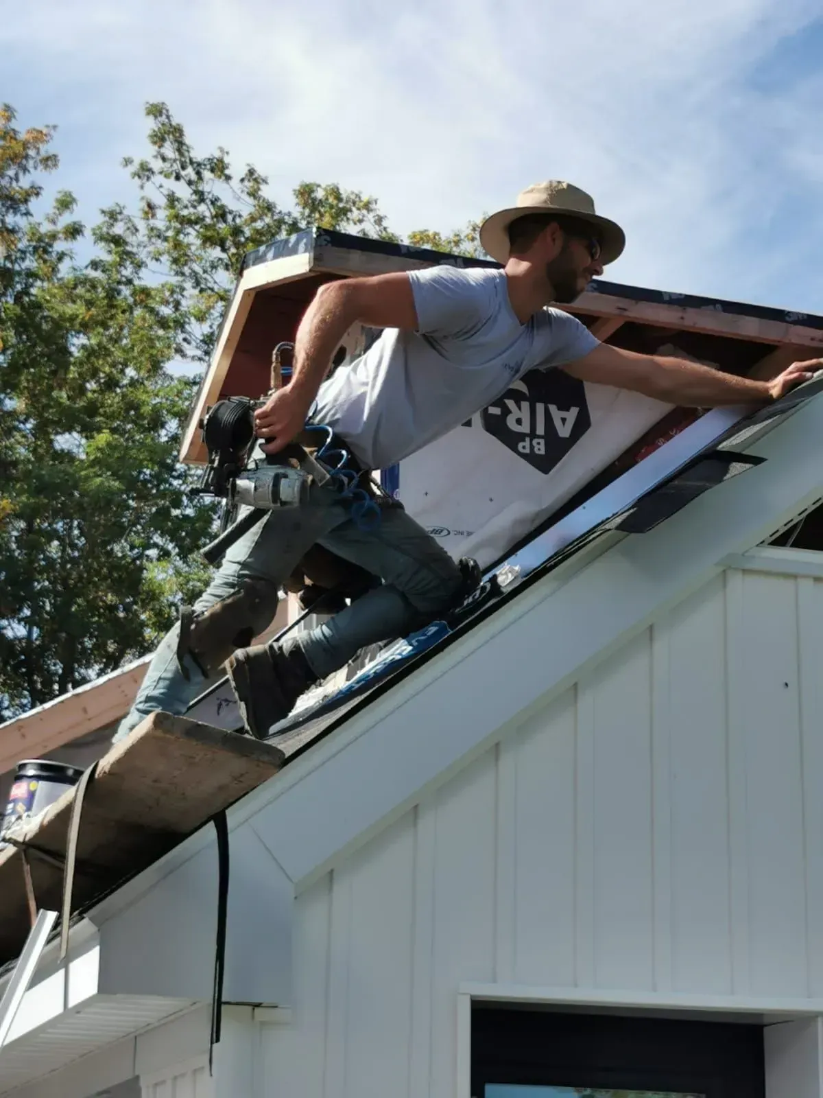 Ouvrier sur le toit d'une maison blanche, installant des bardeaux près d'une cheminée.