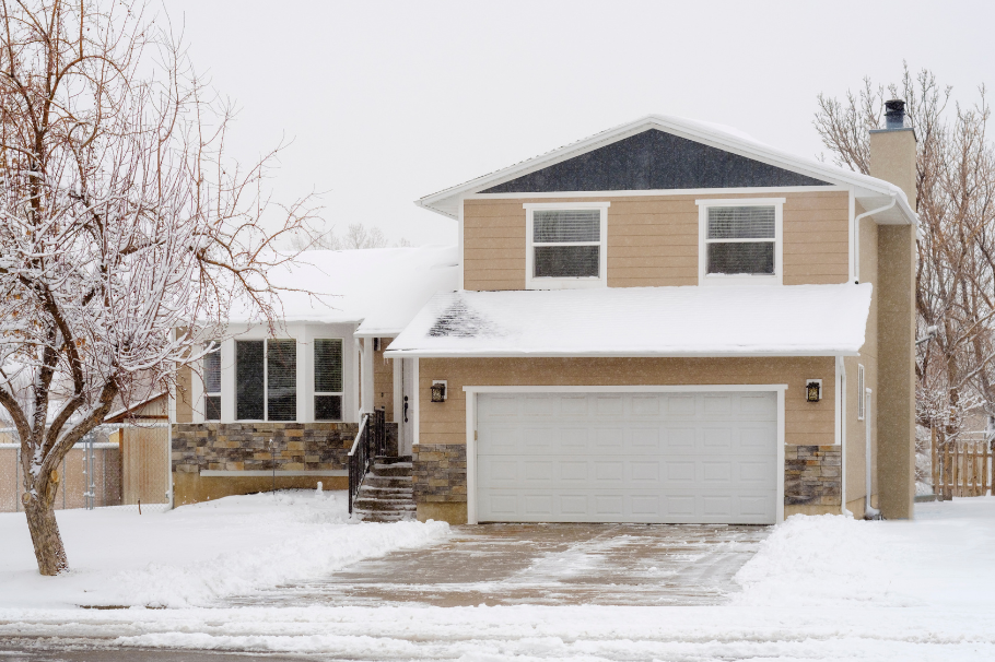 A suburban home with a well-maintained concrete driveway in light snow. Cleared pathways highlight w