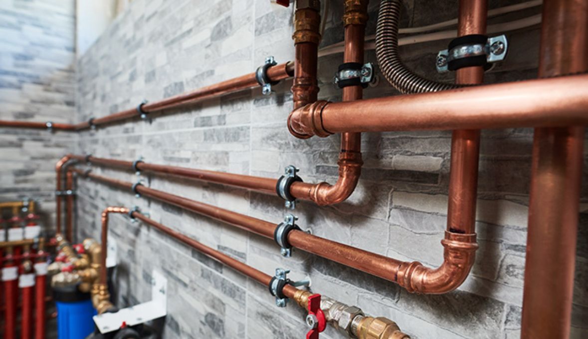 Copper pipes and fittings installed on a gray brick wall.