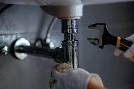 Plumber tightening a chrome sink drain pipe under a sink with a wrench
