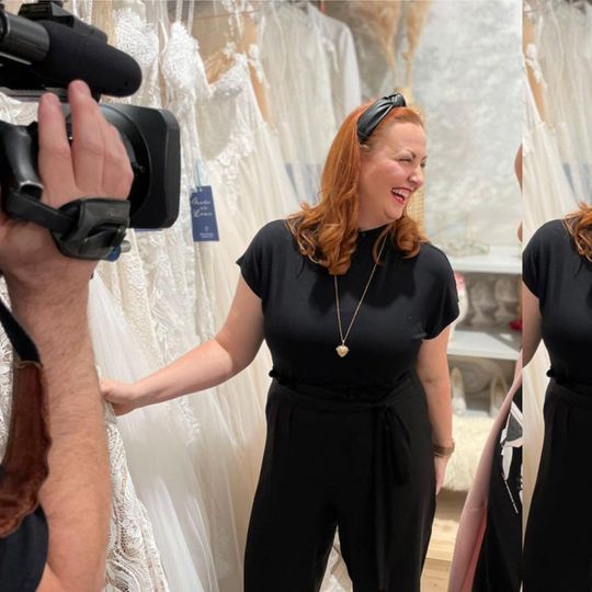Eine Frau in einem schwarzen Kleid wird von einem Kameramann gefilmt