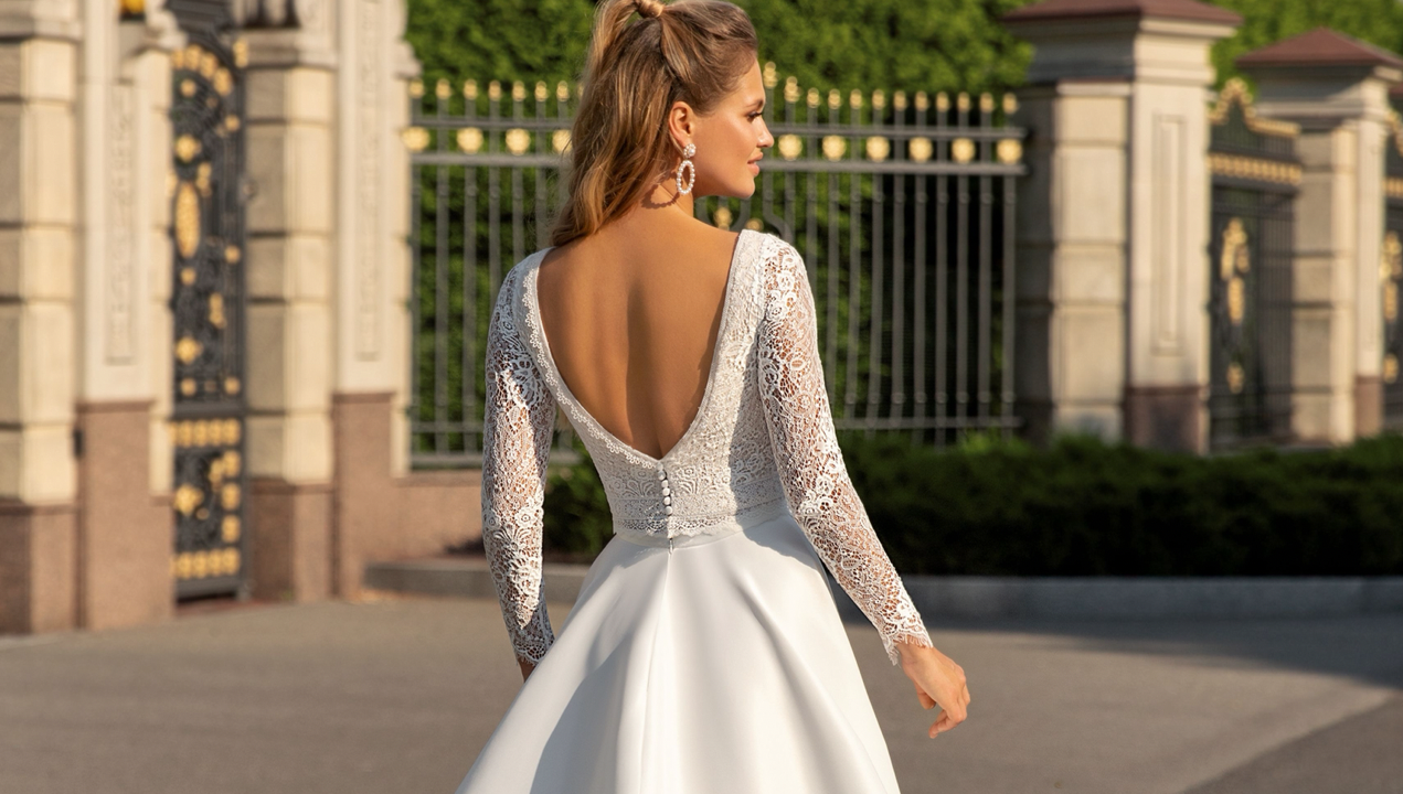 Eine Frau in einem weißen Brautkleid mit langen Ärmeln geht die Straße entlang.