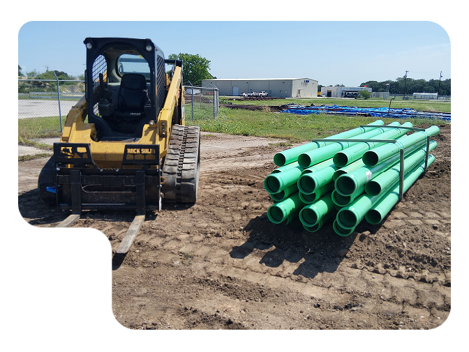 Yellow excavator beside stacked green pipes at a construction site.