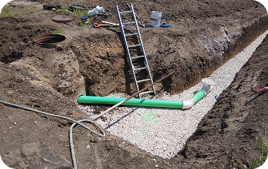 Trench with gravel bedding, green pipe, and a ladder in an excavation site