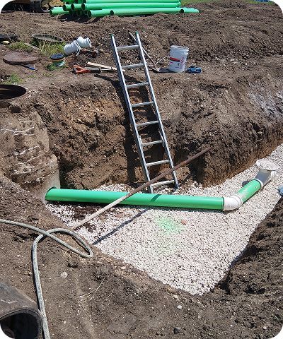 Construction trench with ladder and green pipes over gravel foundation area