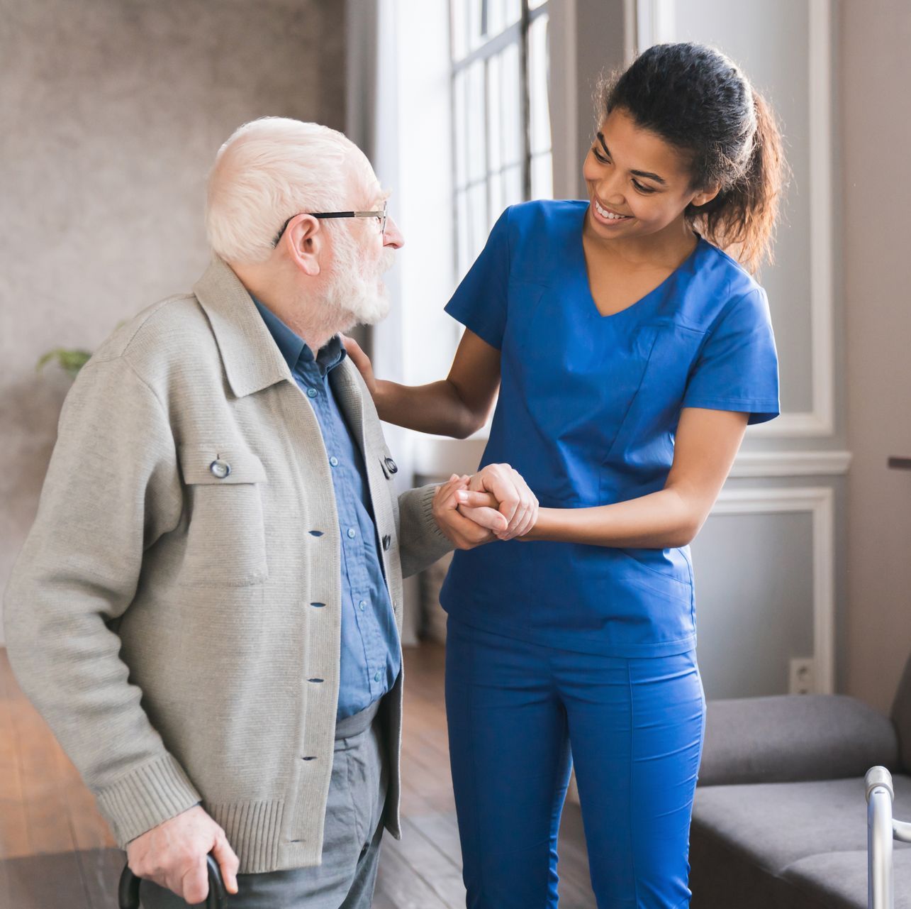 A nurse is helping an elderly man walk with a cane.
